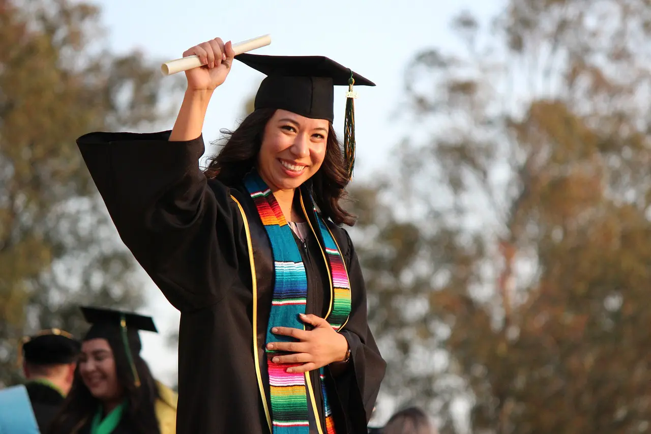 A woman in graduation gown holding up her cap.