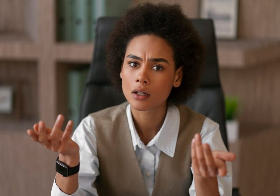 Confused person gesturing with hands at desk.